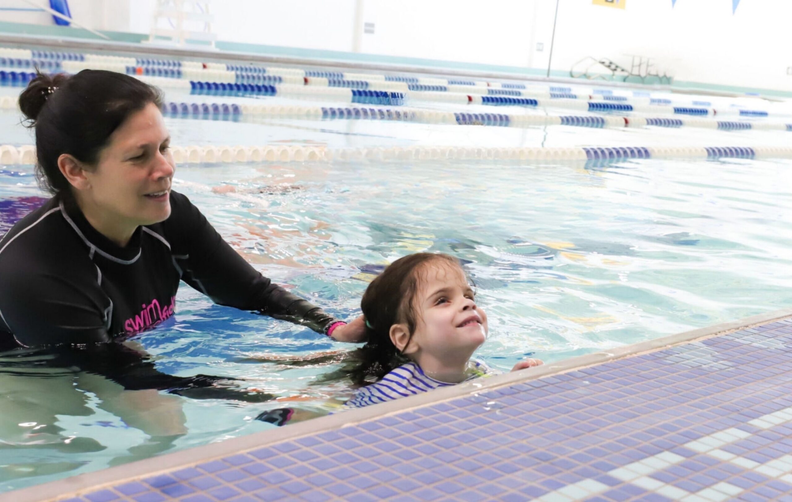 Swim instructor providing tactile arm guidance to a backstroke swimmer with visual impairment.